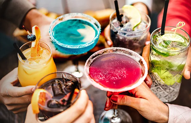 people doing a cheers with colorful alcoholic drinks